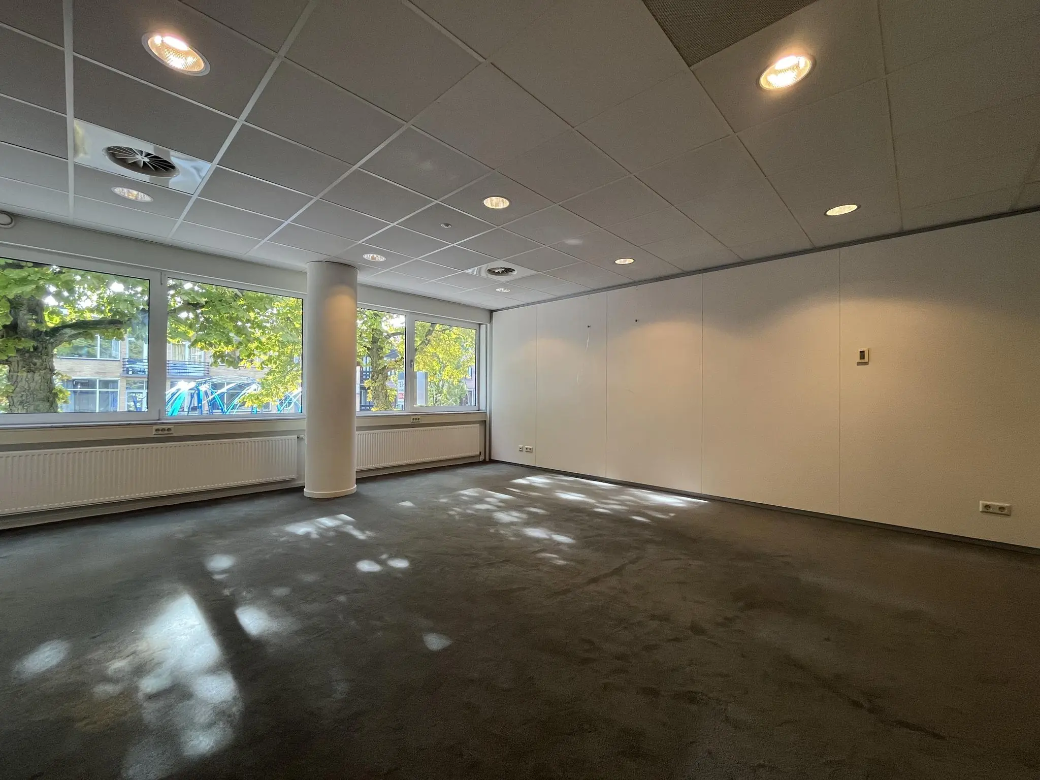 Licht kantoorruimte aan de 1e Hogeweg met grote ramen en uitzicht op bomen.